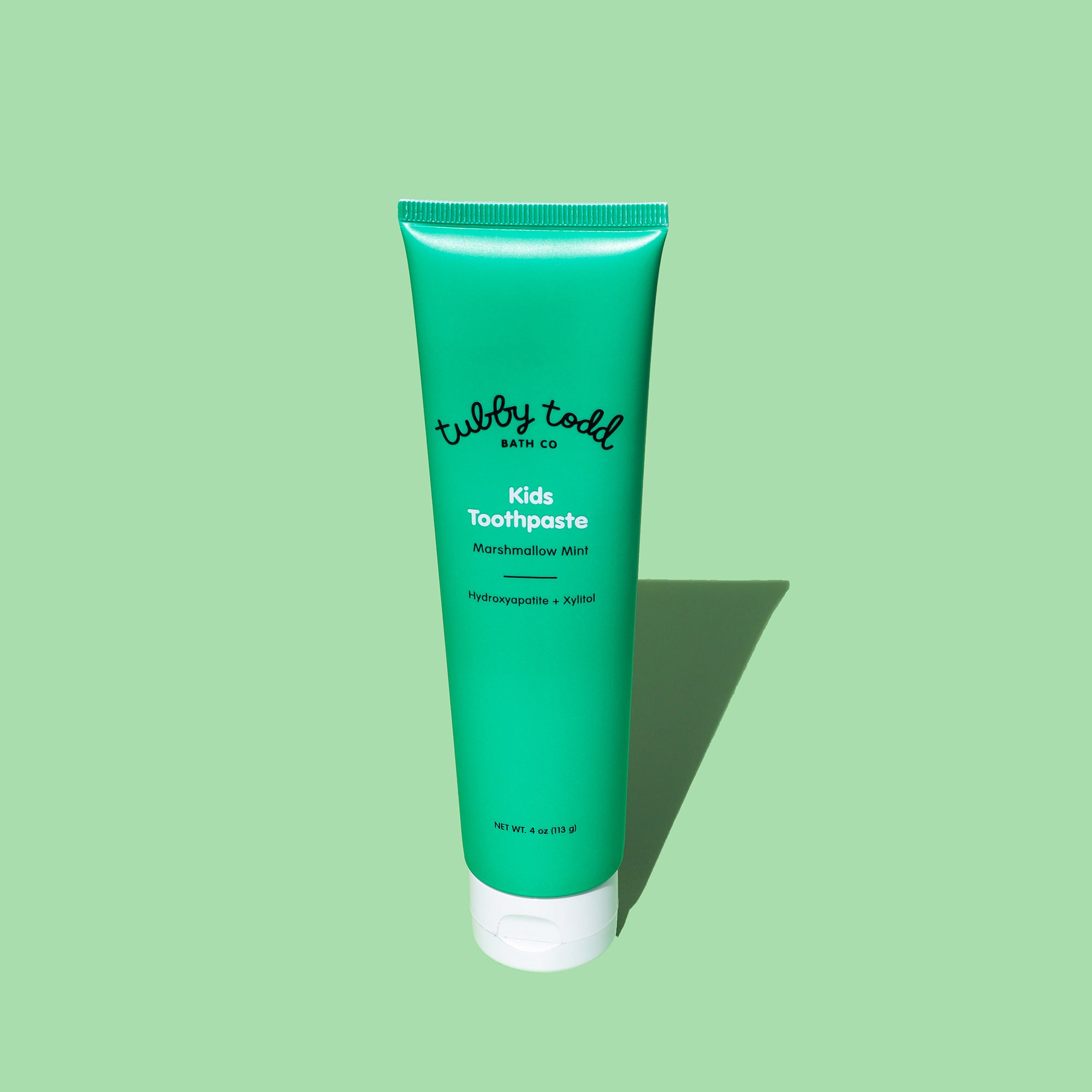 Green tube of Marshmallow Mint kids toothpaste on a light green background